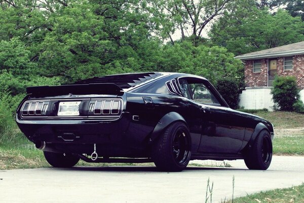 A black Mustang car pulls into the parking lot next to the house