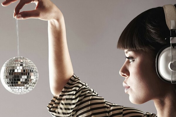 Brunette with bangs in headphones holds a small disco ball