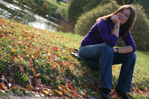 A girl is sitting on the grass with autumn leaves