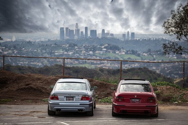 Ein roter und blauer bmw hinter einer Leitplanke im Hintergrund der Stadt hinten