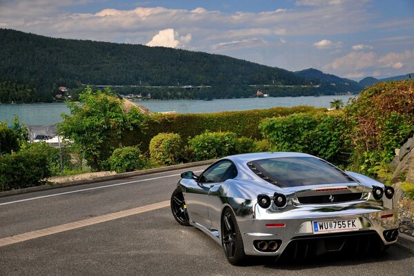 Mirror-silver Ferrari on the highway against the backdrop of a picturesque harbor