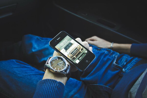 Die Hand mit der Uhr und dem Telefon liegt in Jeans auf den Beinen