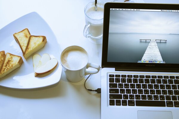 Trabajando en una computadora portátil con una taza de capuchino y postre