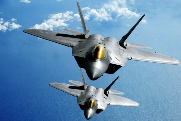 Two military f-22 fighter planes fly over the ocean