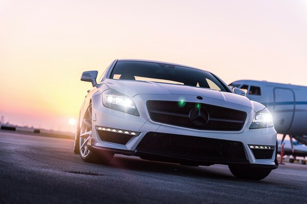 Mercedes de color blanco en el aeropuerto contra el telón de fondo del avión