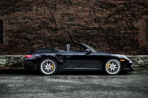 Black sports car convertible along a brick wall