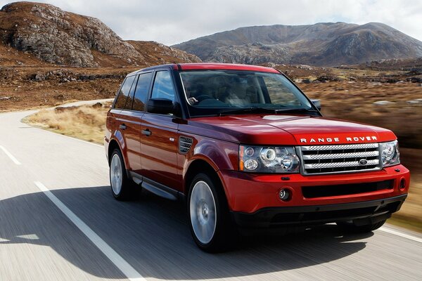 Voiture rouge Renge Rover sur la route sur fond de montagnes