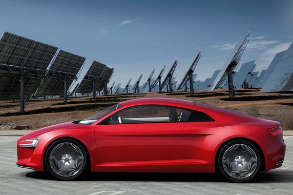 Coche Audi rojo de lado en el campo con paneles solares