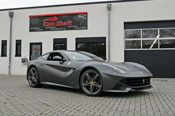 Szare ferrari F12 berlinetta na tle niemieckiego serwisu samochodowego