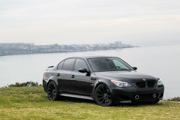 Sport sedán BWM m5 en la orilla del mar se encuentra en el césped