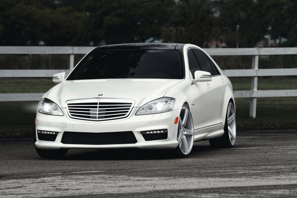 White Mercedes ES class on the background of a white fence