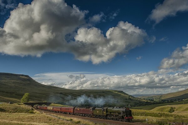 Tren con locomotora de vapor en un hermoso terreno con nubes