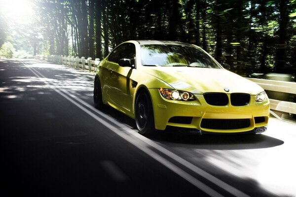 Дорога в лесу и летящей по ней жёлтый BMW