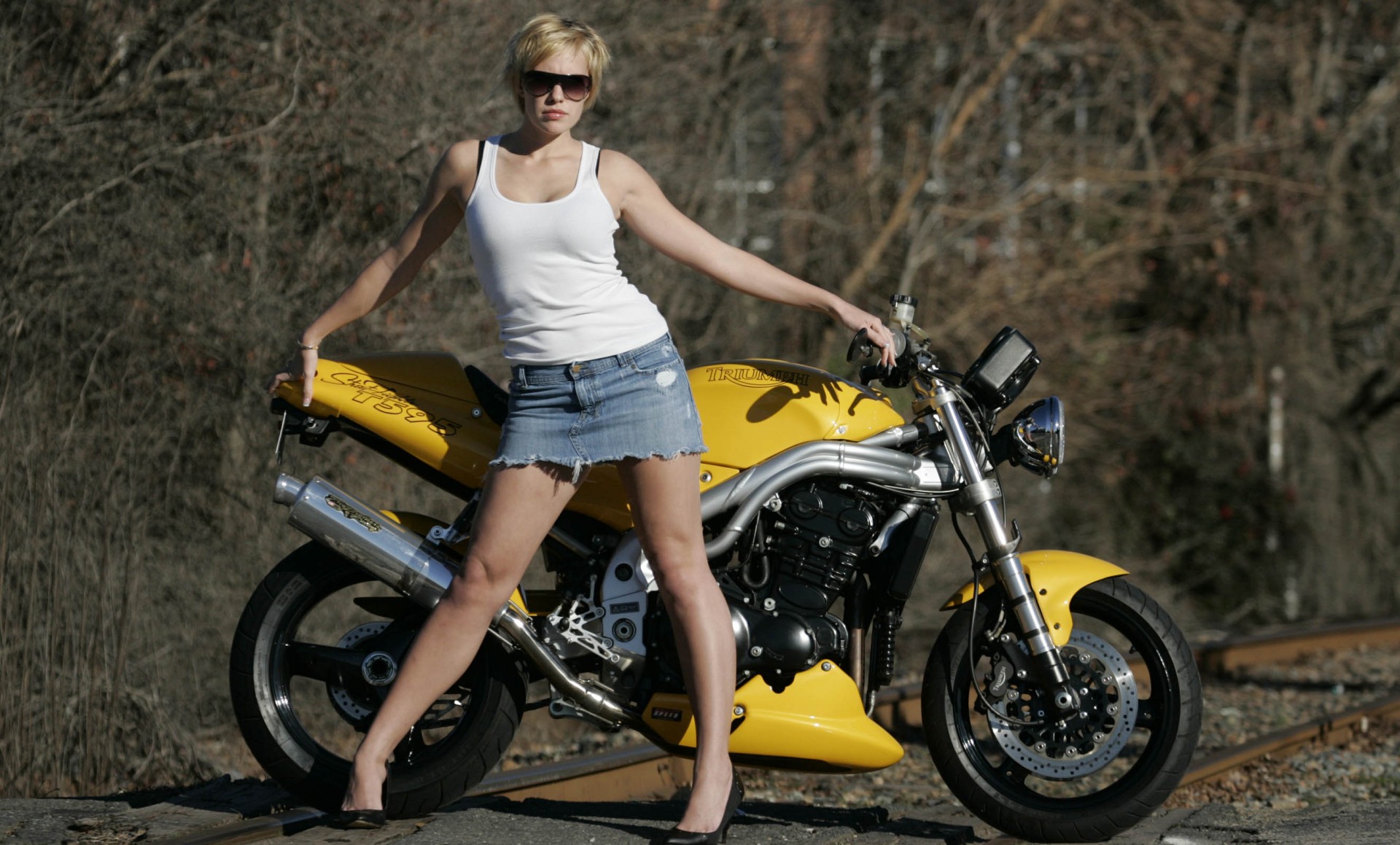 A girl in a denim mini skirt next to a yellow motorcycle wallpaper.