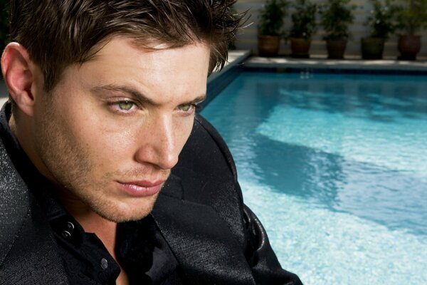 A green-eyed unshaven guy in a shirt near a pool with water