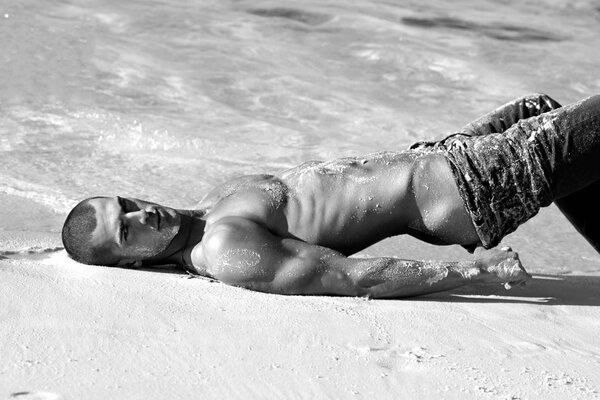 Photo en noir et blanc d un beau mec musclé dans une pose érotique sur le sable
