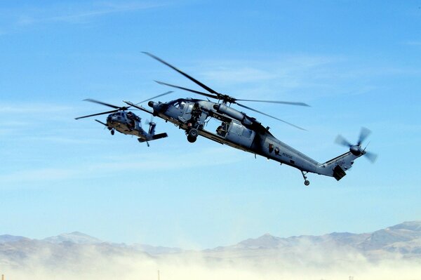 Zwei Hubschrauber fliegen im Dunst über die Berge