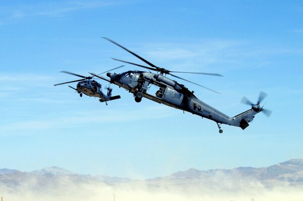 Two helicopters fly over the mountains in a haze