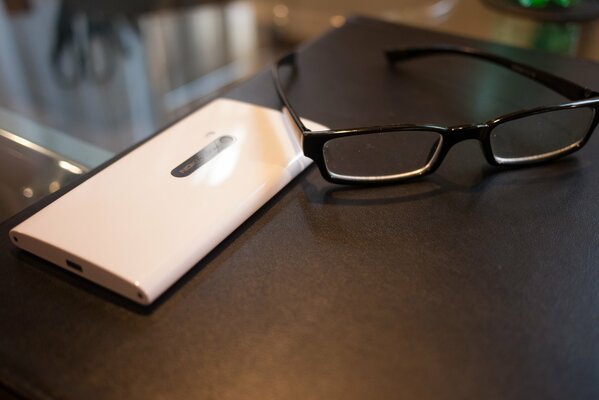 Okulary z białym smartfonem na krawędzi biurka