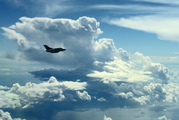 A military plane is flying in the sky among the clouds