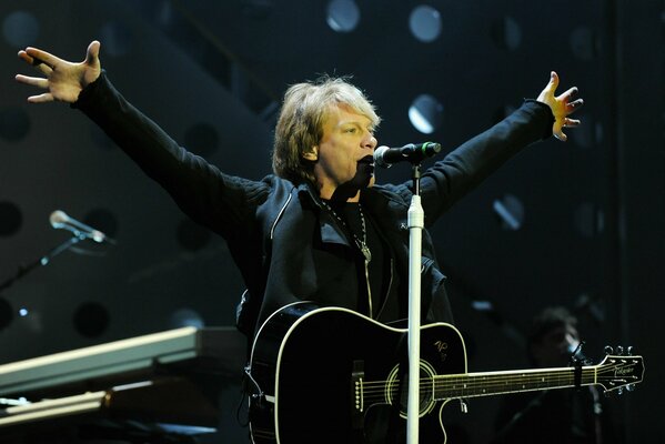 A man with a guitar sings on stage into a microphone