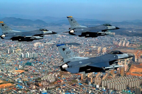 Three fighter jets are flying over the city