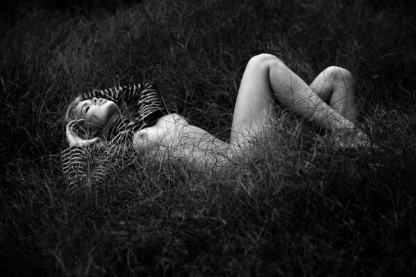 Czarno-białe zdjęcie nagiej dziewczyny leżącej w trawie