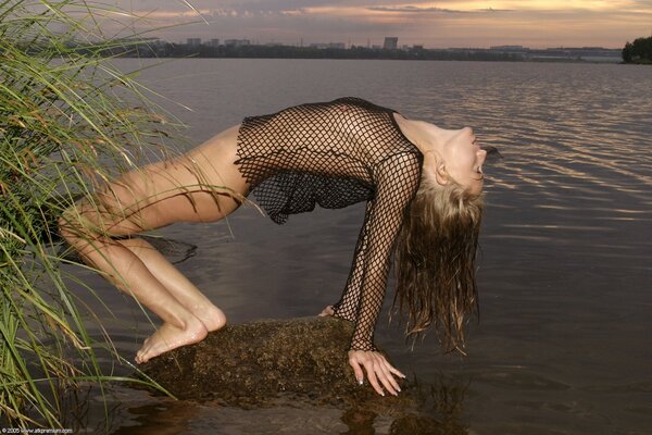 Naked girl in a mesh shirt, posing sexually against the background of the river