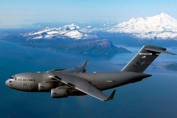 A c - 17 military aircraft flies against the background of mountains