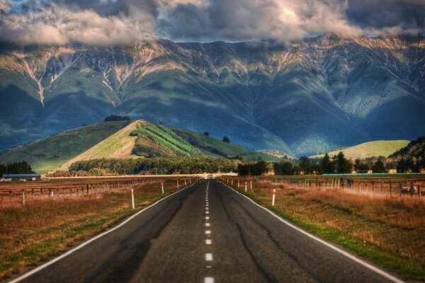 A road surrounded by fields with views of the hills and mountains of New Zealand