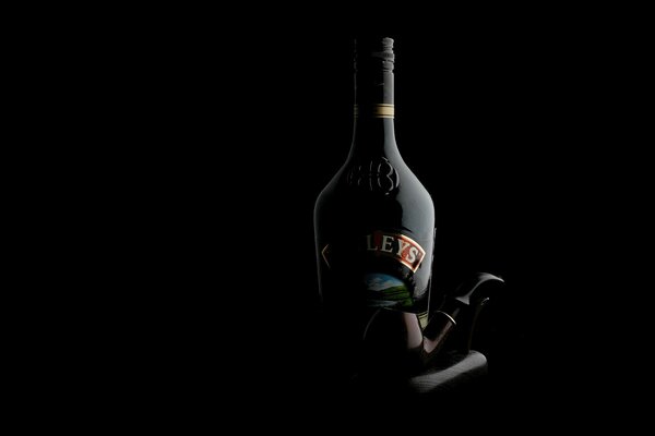 A bottle of liquor and a pipe on a dark background