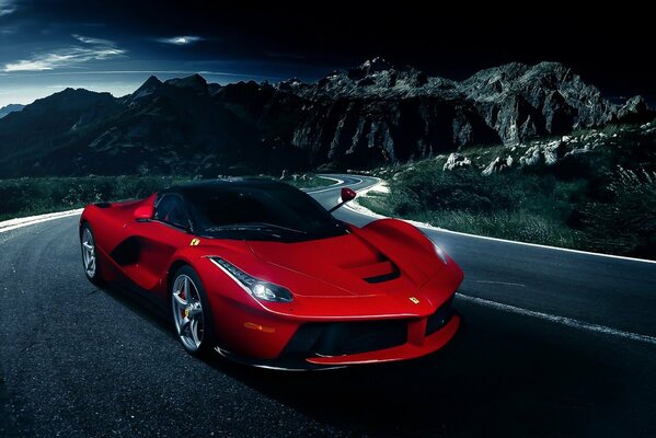 A red Ferrari is driving on a mountain road at night