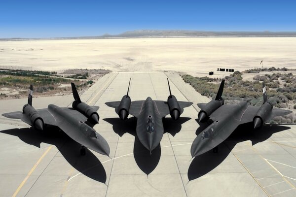 Three black fighter jets are standing on the runway