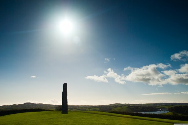 A stone pillar on a hill. the sun in the sky