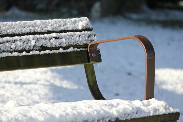 Заснеженная скамейка зимой в парке