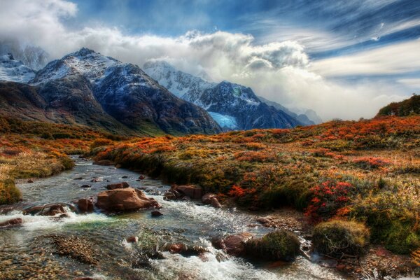 Las nubes caen sobre las montañas. Paisaje con flores de montaña y río