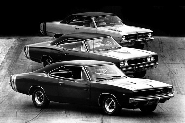 Foto en blanco y negro, tres coches de la época: dos dodge y un muscle Car