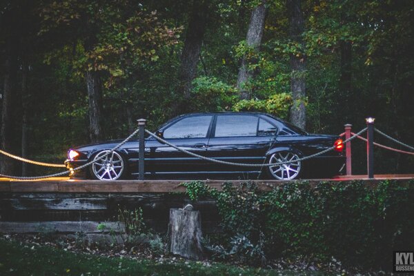 BMW E38 740iL noir sur le pont avec les phares allumés vue latérale