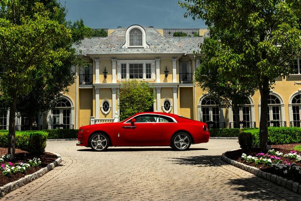 Rolls-Royce2015 in bright red color stands in the park near the house