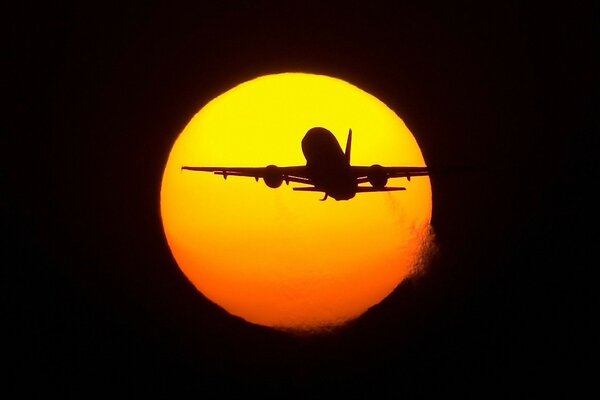 The plane flies against the background of the sun