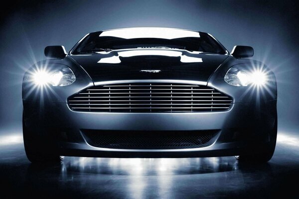 A black and white image of an Aston Martin with its headlights on. Aston Martin front view with headlights on