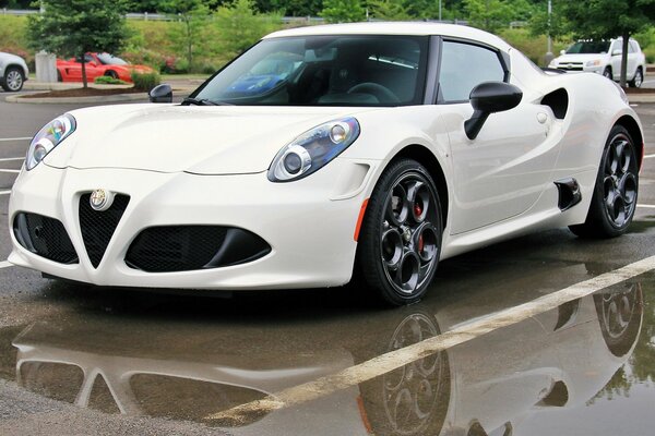 White Alfa Romeo 4s reflected in the mirror of the wet asphalt of the parking lot