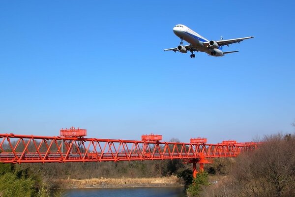 Samolot pasażerski lecący nad czerwonym mostem