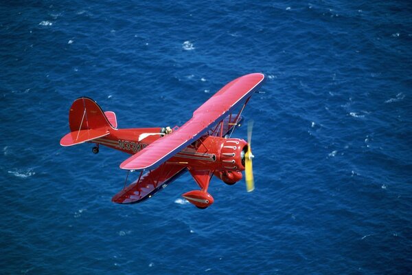 Roter Doppeldecker fliegt über das Meer