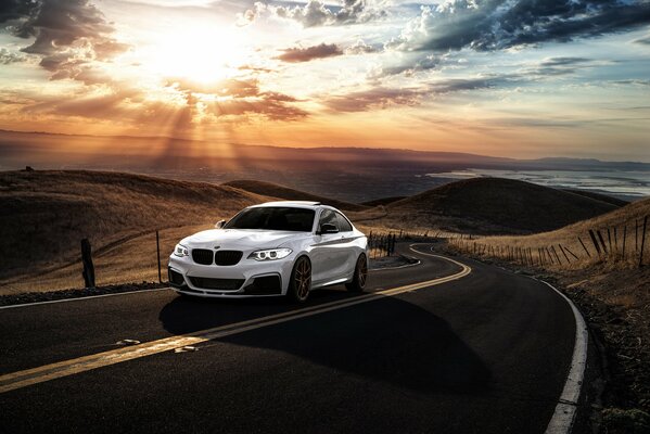 Białe BMW ściga się górską drogą San Jose, z dala od malowniczego zachodu Słońca