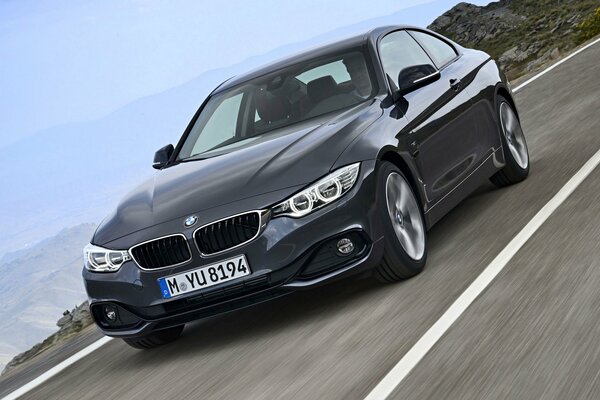 Black bwm of the fourth series rides on a road with a beautiful landscape