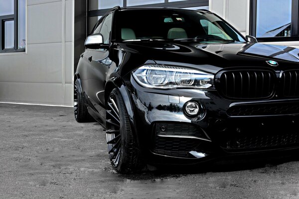 A tuned black BMW X5 is parked outside the building