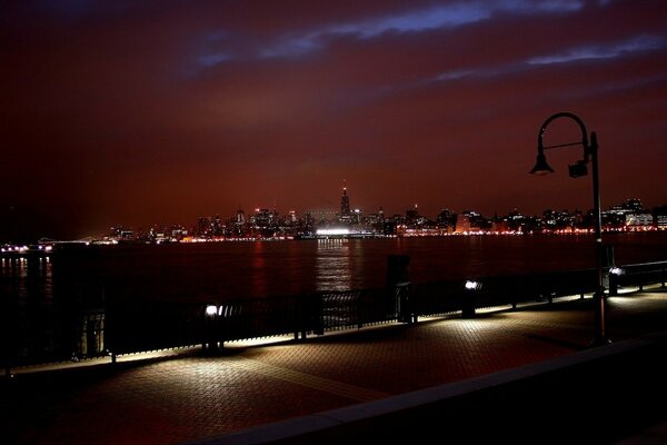 Тусклое освещение в нью-йорком городе на берегу реки стоят скамейки