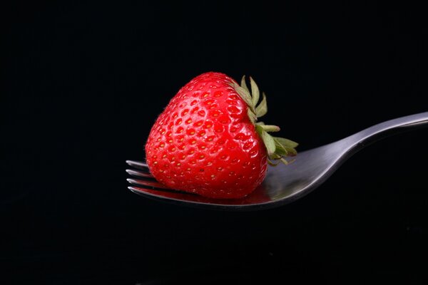 Red strawberries on a fork on a black background