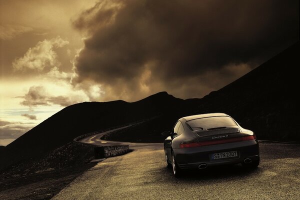 A black sports car rides on a mountain road under a cloudy sky